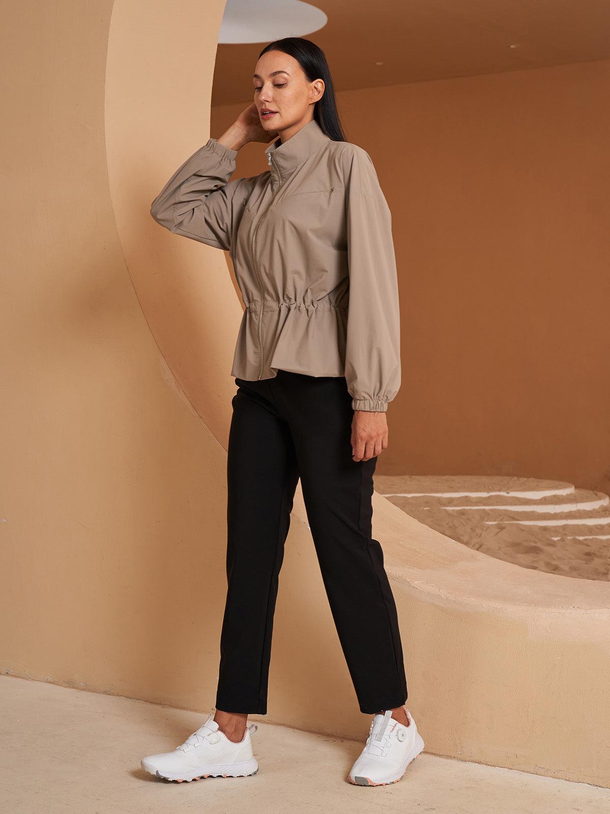 Woman wearing a beige lightweight golf jacket and black performance trousers.