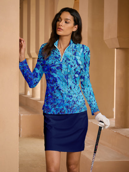 Woman wearing a blue patterned long-sleeve golf polo and navy golf skirt holding a golf club.