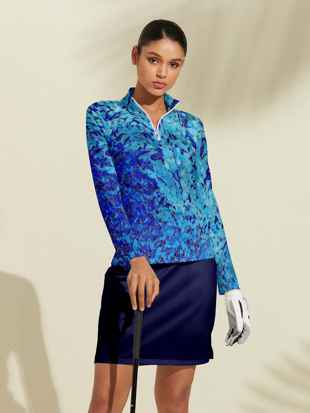 Woman wearing a blue abstract print long sleeve golf pullover and navy golf skirt.