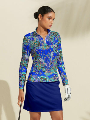 Woman wearing a blue paisley print long sleeve golf top and navy blue golf skirt.