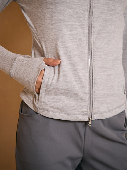 Woman wearing a light grey performance zip-up golf jacket and grey athletic trousers.