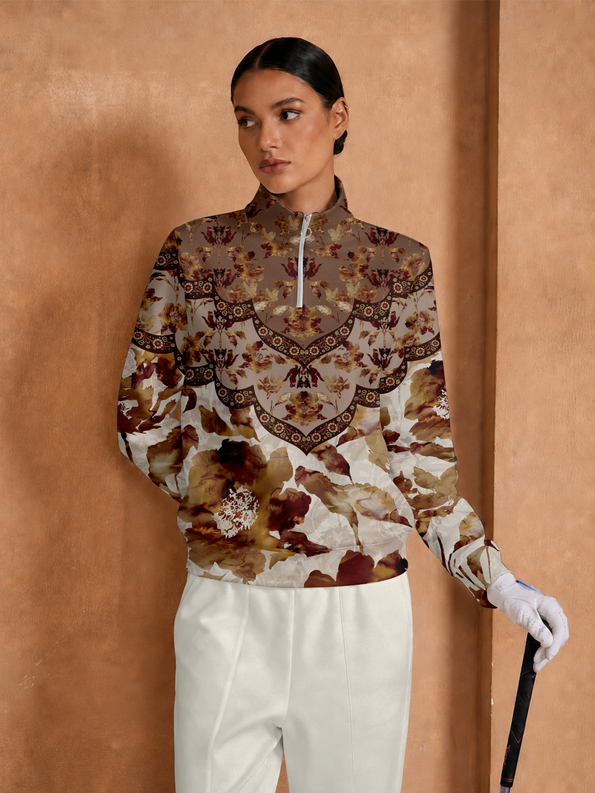 Woman wearing a floral print long sleeve golf pullover and white trousers.