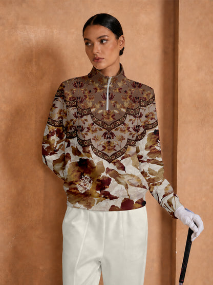 Woman wearing a floral print long sleeve golf pullover and white trousers.