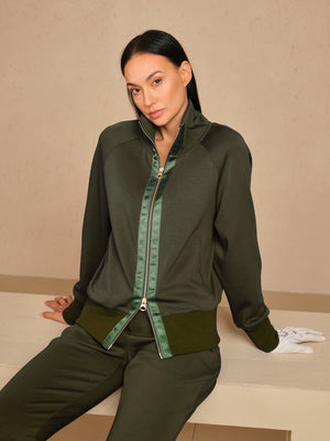 Woman wearing a dark green zip-up golf jacket and matching performance trousers.