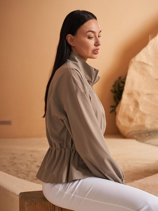 Woman wearing a stylish beige long-sleeve golf jacket and white trousers.