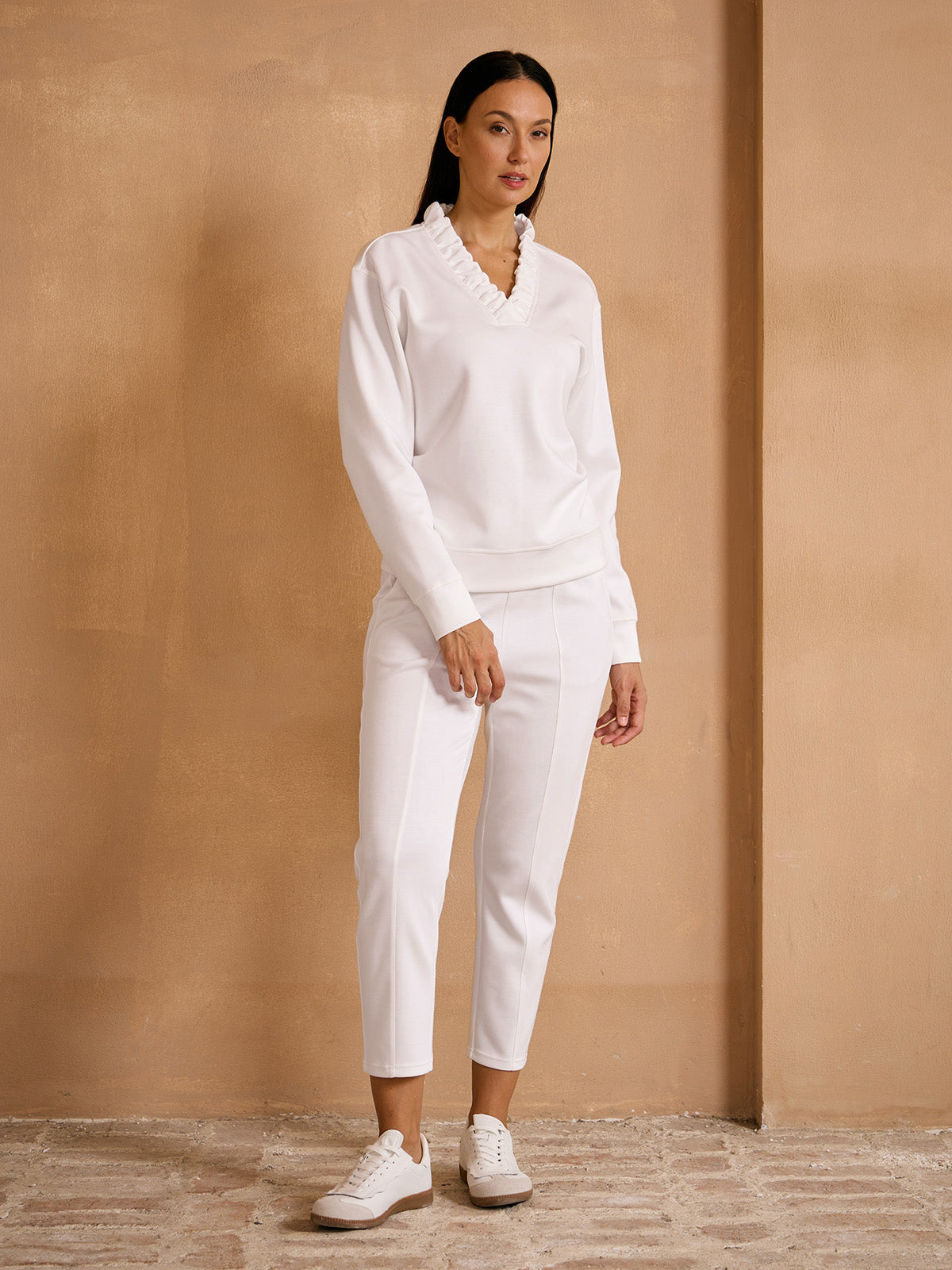 Woman wearing a white long-sleeve ruffled sweatshirt and matching white golf trousers.
