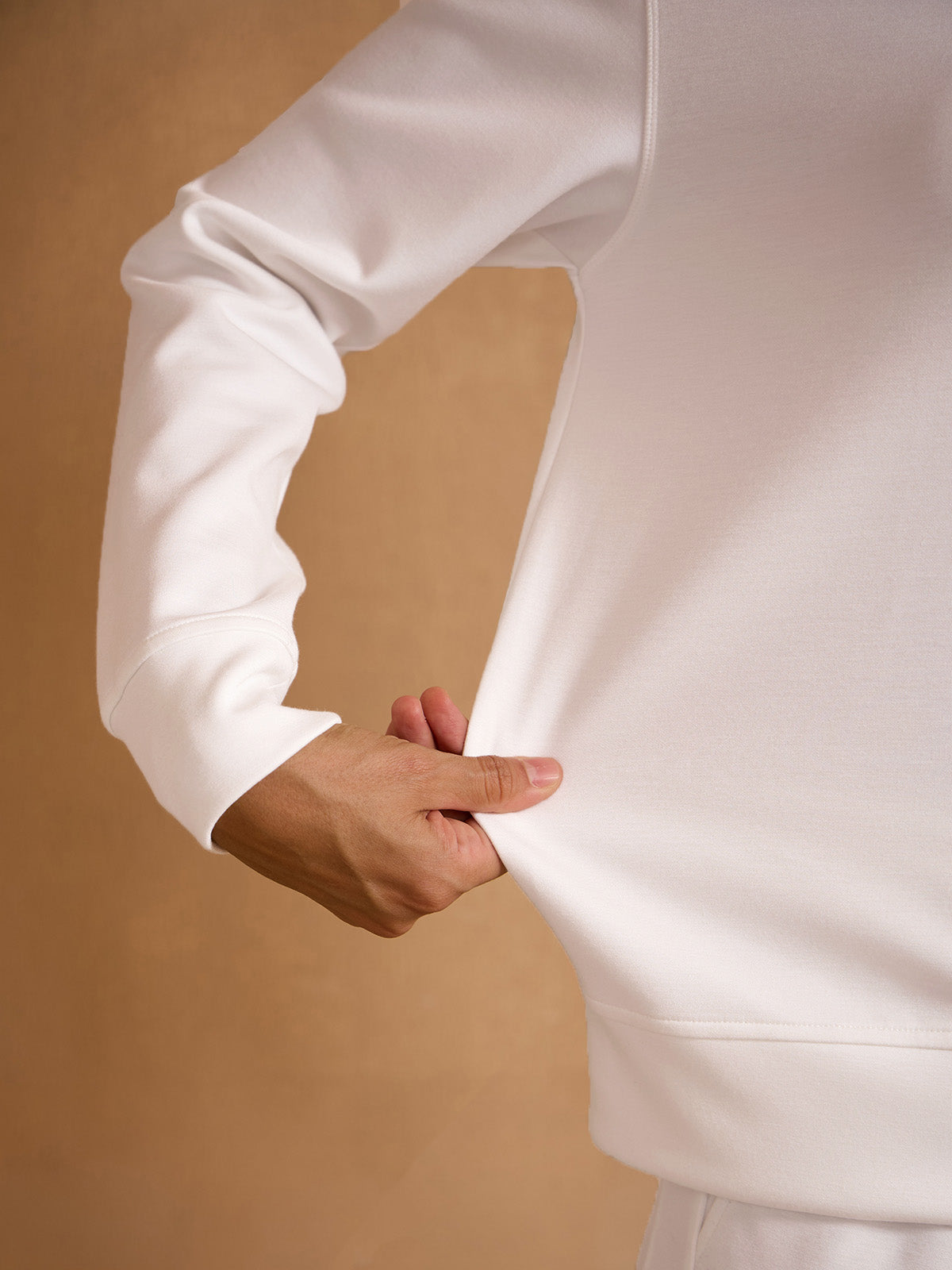 Close-up of a person demonstrating the flexible fabric of a white performance golf sweatshirt.