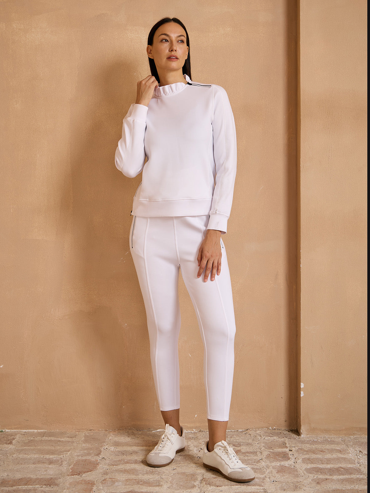 Woman wearing white performance golf sweatshirt and matching leggings.