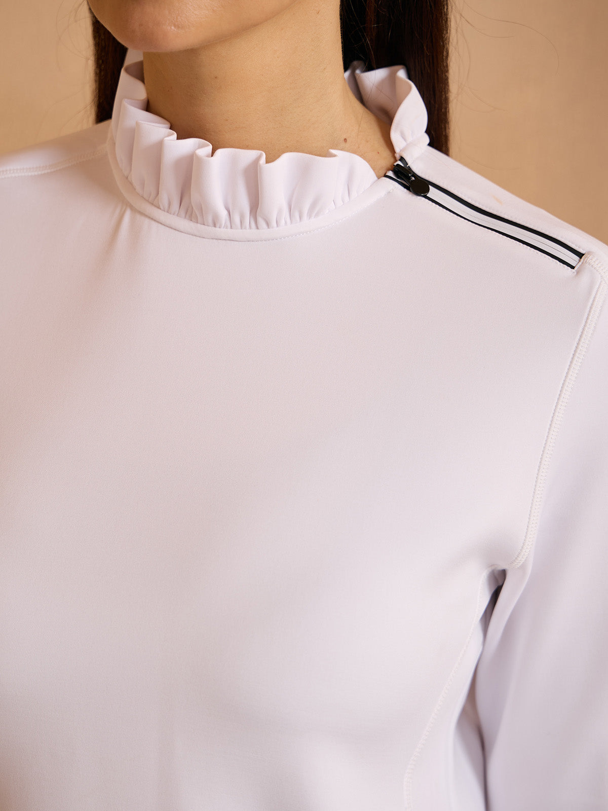 Close-up of a woman wearing a white performance golf top with a ruffled collar and zipper detail.