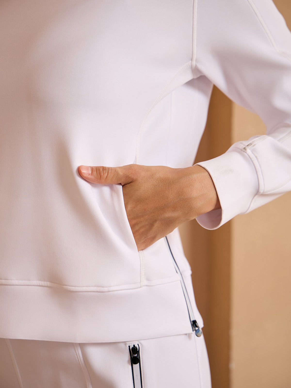 Woman wearing a white performance golf jacket with a side pocket.