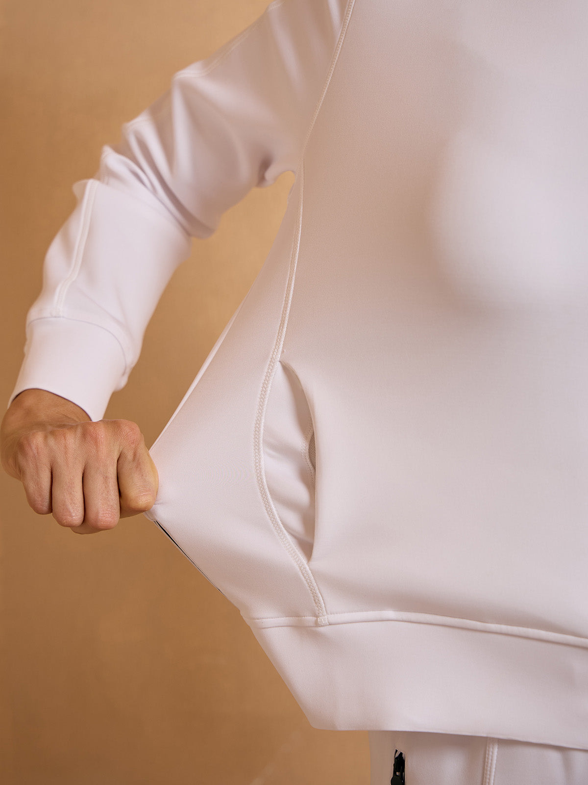 Woman wearing a white performance golf sweatshirt with a functional side pocket.