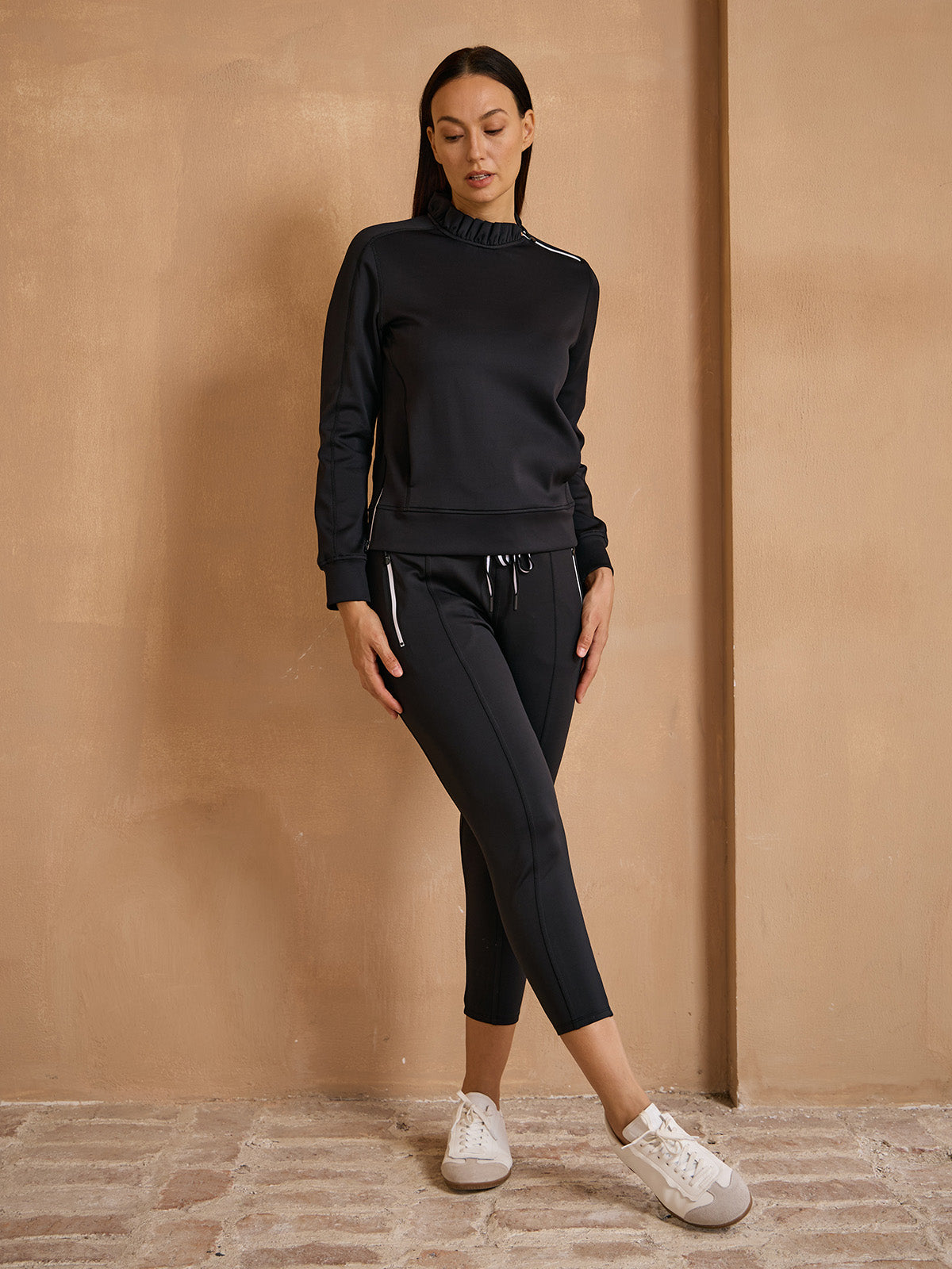 Woman wearing a black long-sleeve performance sweatshirt and matching cropped athletic leggings.