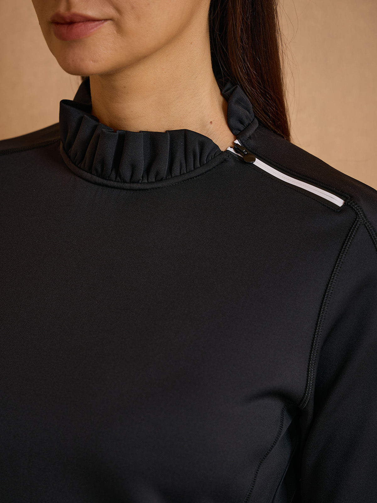 Woman wearing a black high-neck performance golf top with ruffled collar detail.
