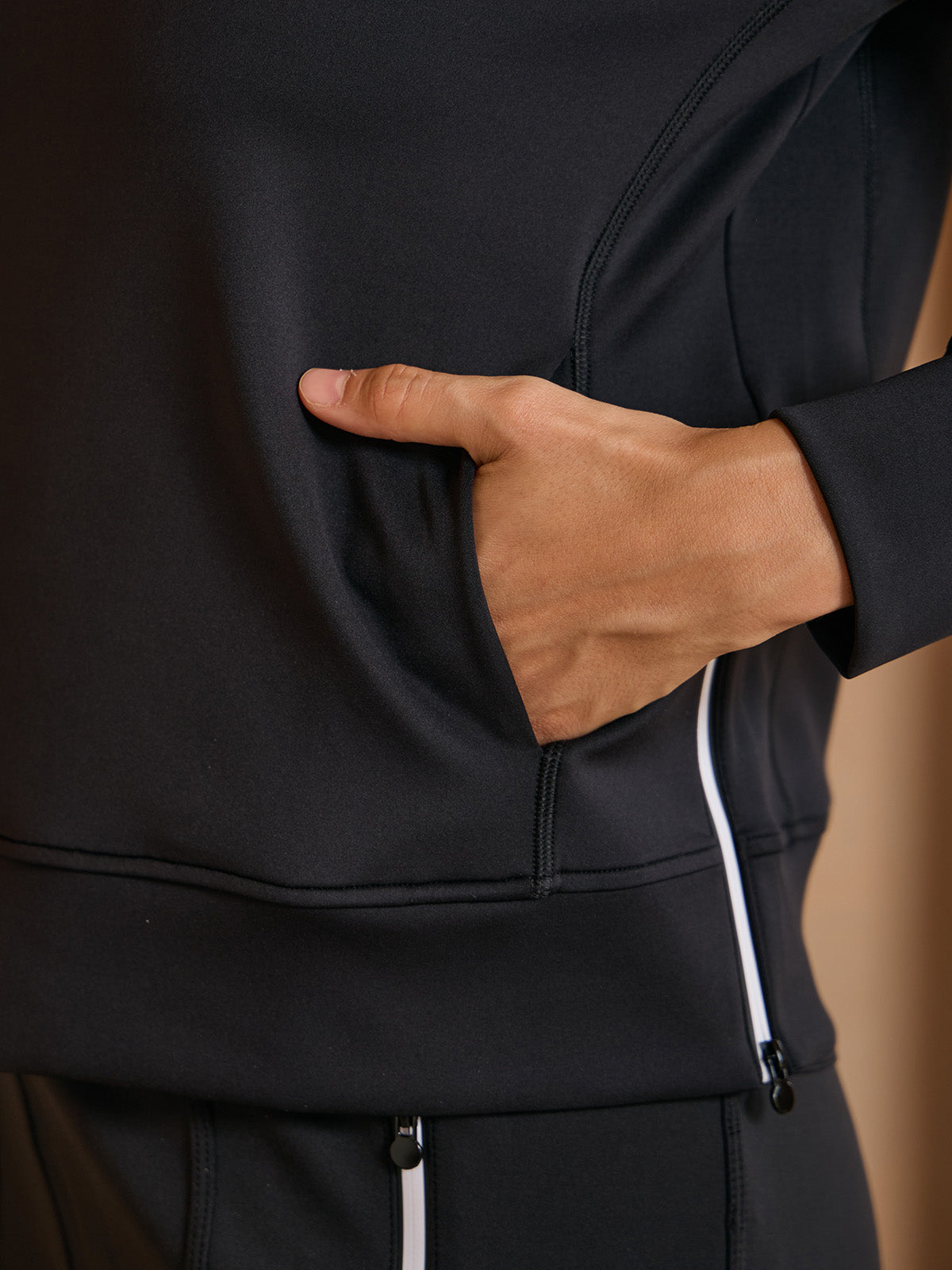 Close-up of a person wearing a black performance golf jacket with a zippered pocket.