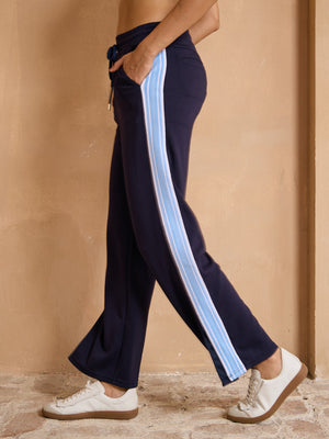 Woman wearing navy blue performance golf trousers with light blue side stripes and white sneakers.