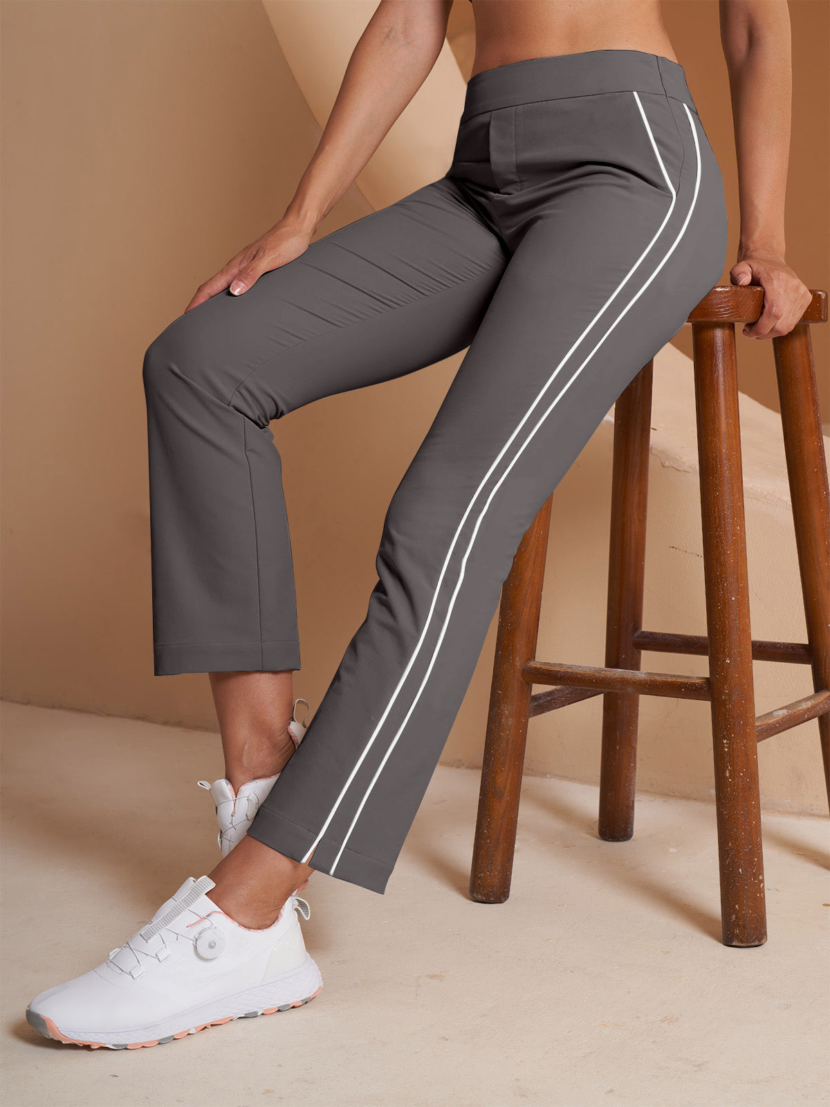 Woman wearing grey performance golf trousers with white side stripes and white golf shoes.