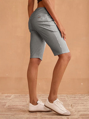 Woman wearing checkered pattern golf skorts and white golf shoes.