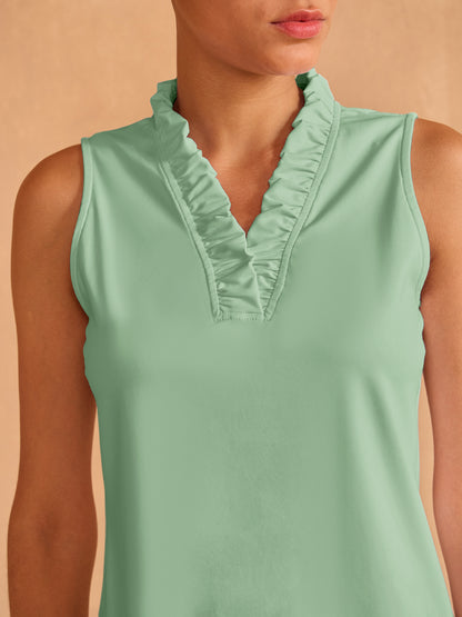 Woman wearing a mint green sleeveless golf polo with ruffle detailing on the neckline.