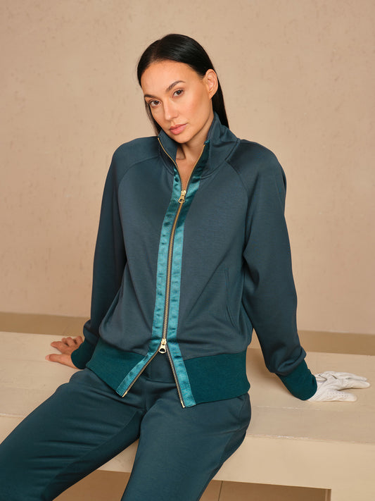 Woman wearing a teal women's golf track jacket and matching performance trousers.
