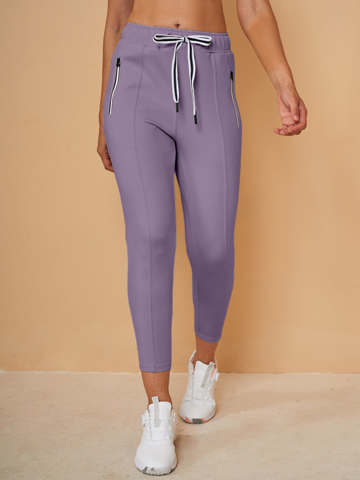 Woman wearing purple cropped golf pants with drawstring waist and zippered pockets.