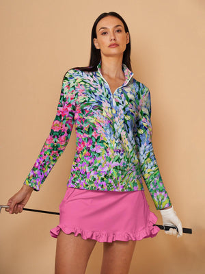 Woman wearing a floral print long sleeve golf top and a pink ruffled golf skirt.
