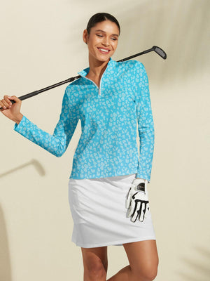 Woman in blue patterned long sleeve golf top and white golf skirt holding a club.
