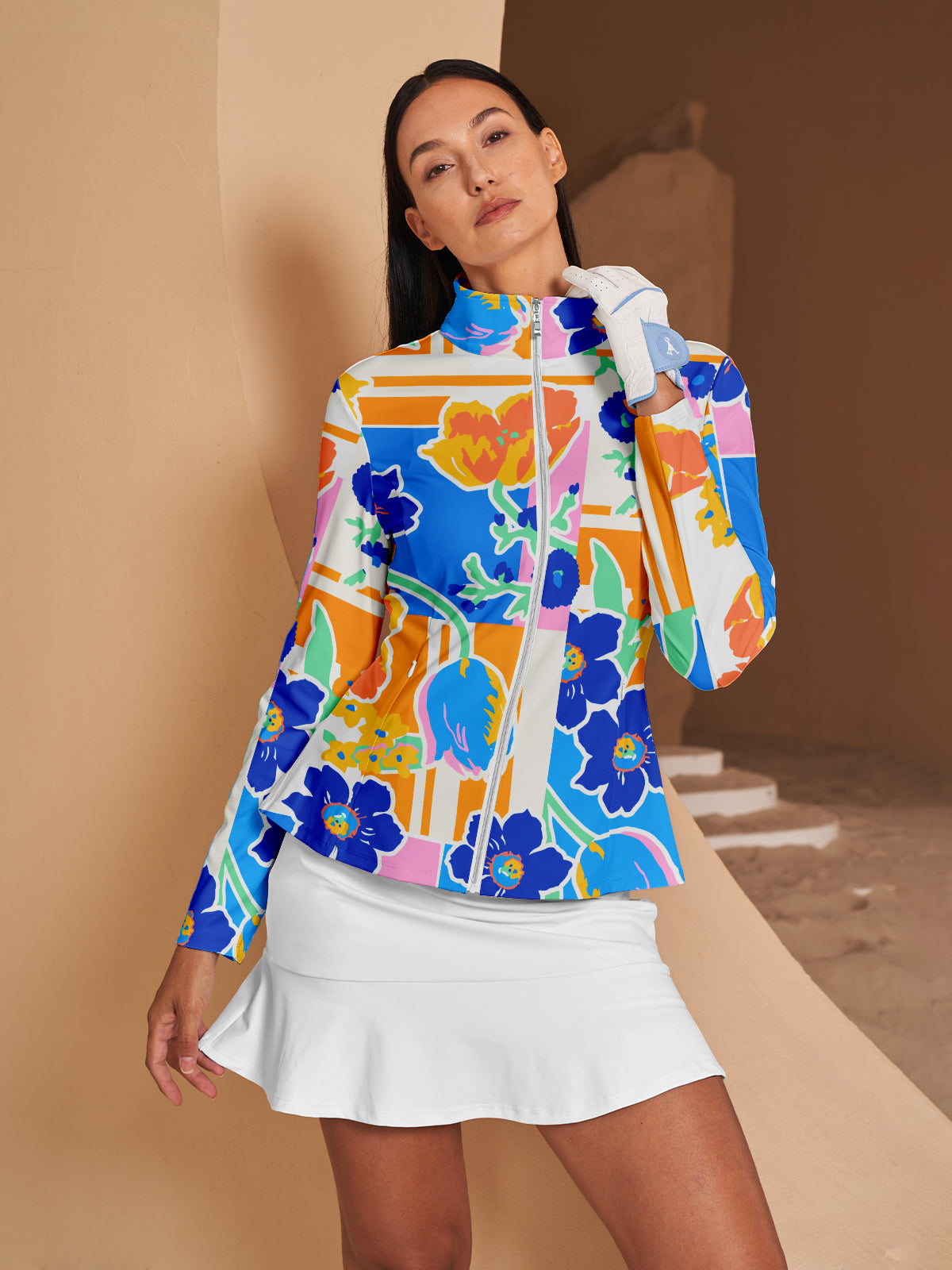 Woman wearing a colorful floral print golf jacket and white golf skirt.