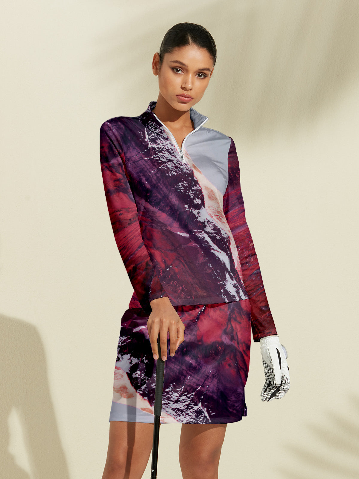 Woman wearing a patterned long-sleeve golf top and matching skirt holding a golf club.