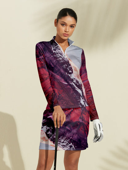 Woman wearing a patterned long-sleeve golf top and matching skirt holding a golf club.