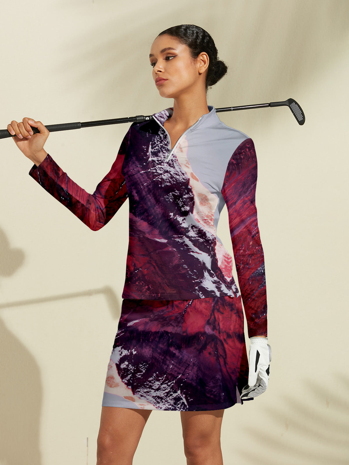 Woman wearing a patterned long-sleeve golf shirt and matching skirt holding a golf club.