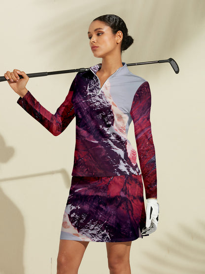 Woman wearing a patterned long-sleeve golf shirt and matching skirt holding a golf club.