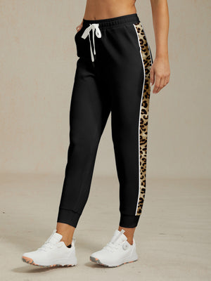 Women's black performance golf joggers with leopard print side stripes and white drawstring.
