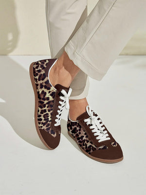 Women's leopard print and brown golf shoes with white laces and white trousers.