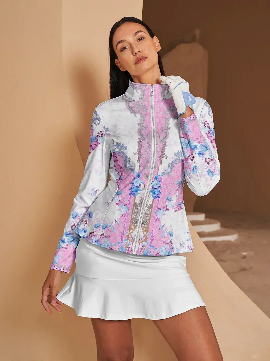 Woman wearing a floral print long sleeve golf jacket and white golf skirt.