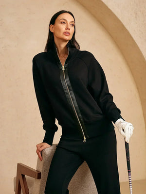 Woman in black athletic zip-up jacket and trousers holding a golf club.