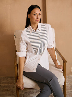 Woman wearing a white long-sleeve golf shirt with striped detail and grey trousers.