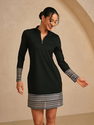 Woman wearing a black long-sleeve golf dress with patterned cuffs and hem.