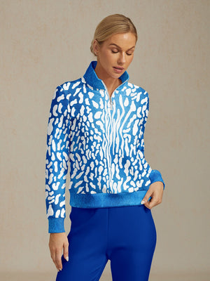 Woman wearing a blue and white patterned zip-up performance golf jacket and blue trousers.