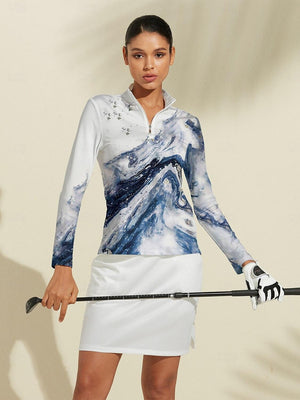 Woman wearing a blue marble print long sleeve golf top and white golf skirt holding a club.