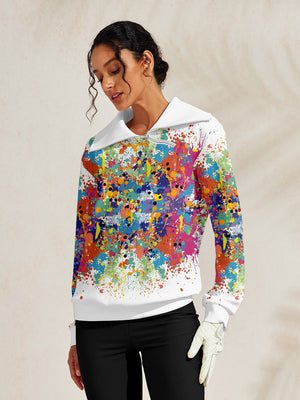 Woman wearing a white long-sleeve golf pullover with colorful paint splatter print.