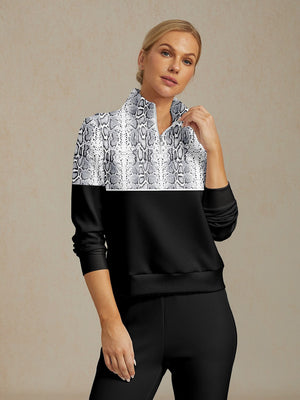 Woman wearing a black and white snakeskin print quarter-zip golf pullover and black pants.