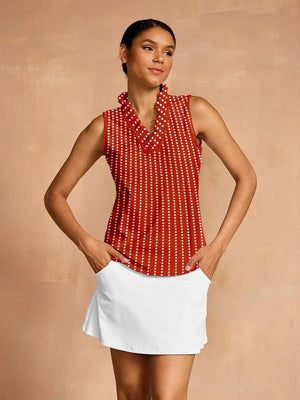 Woman wearing a red and white polka dot sleeveless golf top and a white golf skirt.