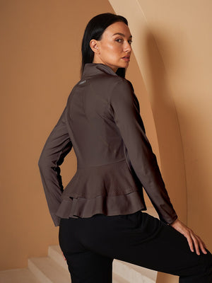 Woman wearing a brown long-sleeve peplum performance golf jacket and black trousers.